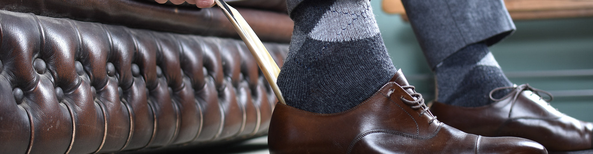 Close-up van stijlvolle, bruine herenschoenen met geruite sokken, zittend op een klassieke leren Chesterfield bank. Verfijnde elegantie in detail.