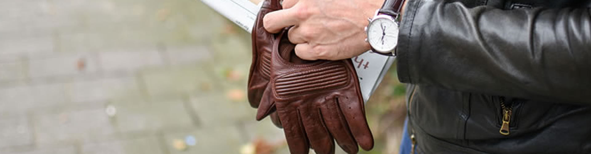 Een close-up van leren Hestra handschoenen, een horloge en een leren jas, suggererend stijlvolle bescherming tegen de elementen.