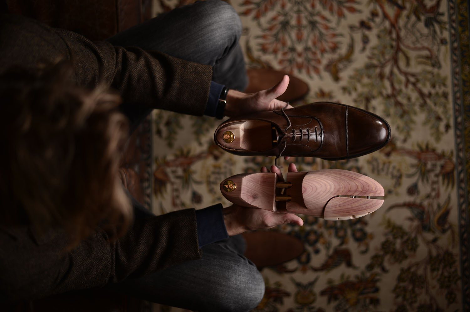 Een man houdt elegante, bruine herenschoenen en houten schoenspanners vast, perfect voor het blog over de juiste schoenmaat.