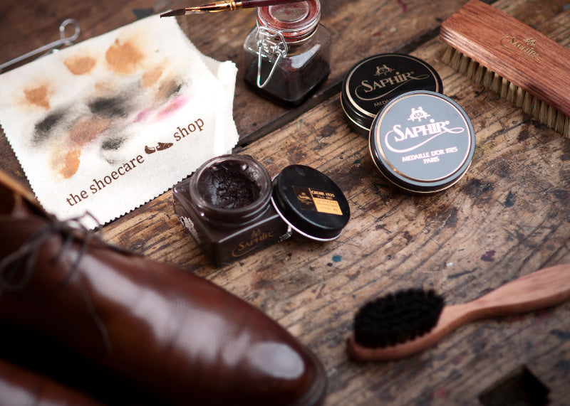 Sfeerbeeld van schoenpoetsen met Saphir Médaille d'Or producten op een rustieke houten tafel, straalt vakmanschap en traditie uit.