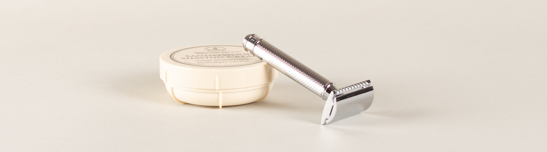 Een klassieke zilveren safety razor leunt elegant tegen een pot sandelhout scheercrème, klaar voor een gladde, nostalgische scheerbeurt.