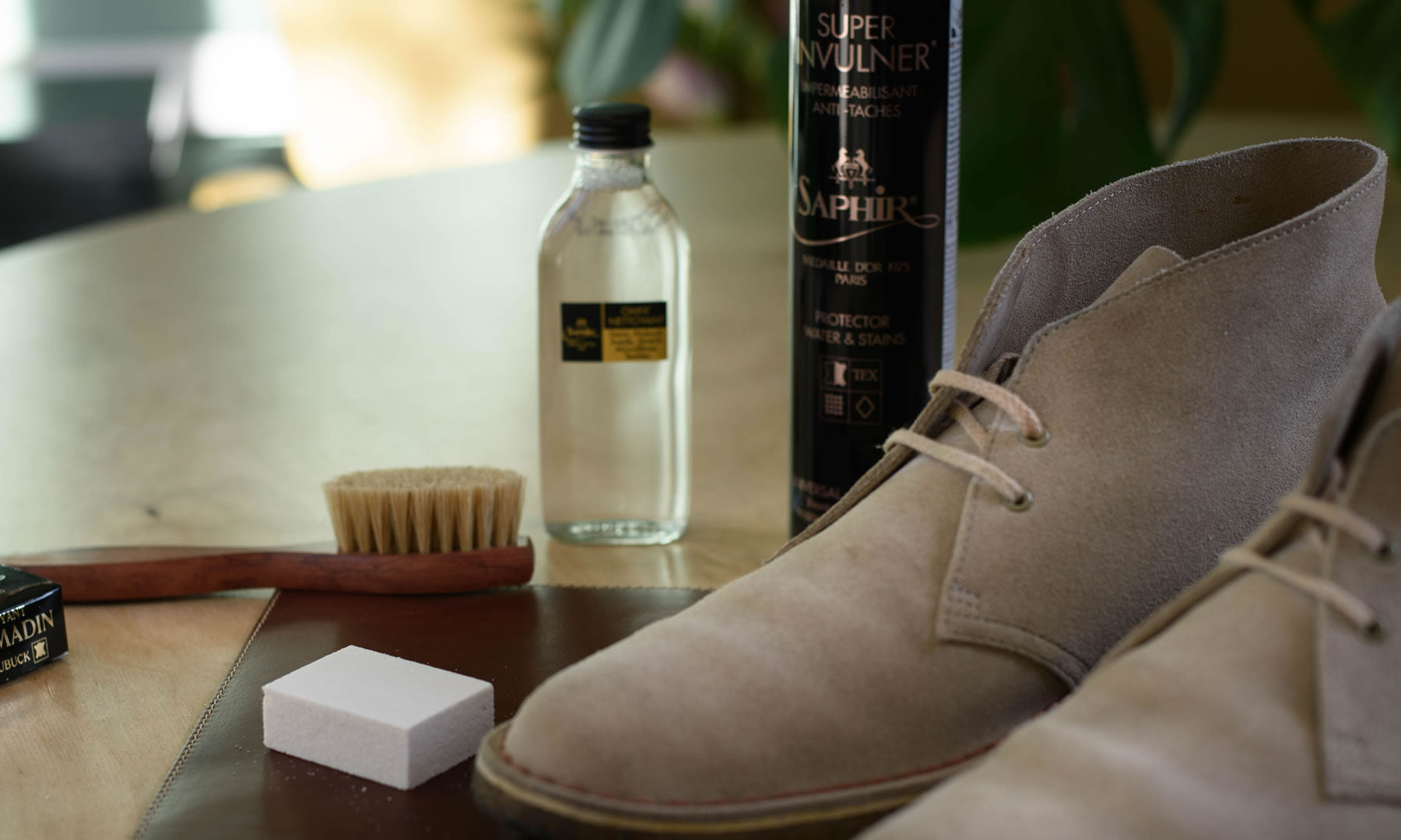 Sfeerbeeld van suède schoenen met reinigingsproducten, borstel en gum, klaar voor een schoonmaakbeurt.
