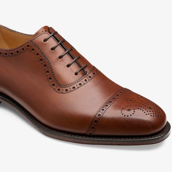 Gedetailleerd beeld van een bruine, leren herenschoen met perforaties en bruine veters op een lichte achtergrond.